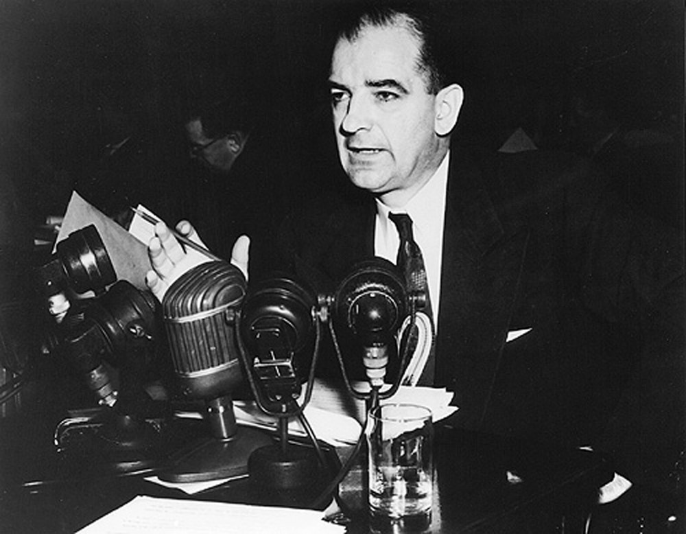 Photograph of Joseph McCarthy, speaking into a half dozen microphones.