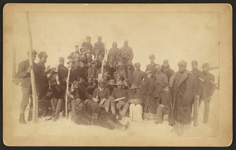 A photograph of twenty-five Black American cavalrymen standing and sitting together. 