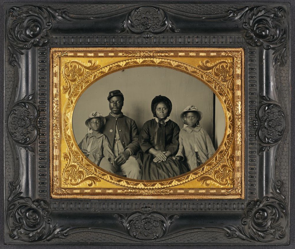 A photograph of an African American family in nice clothes. The father is wearing a uniform.