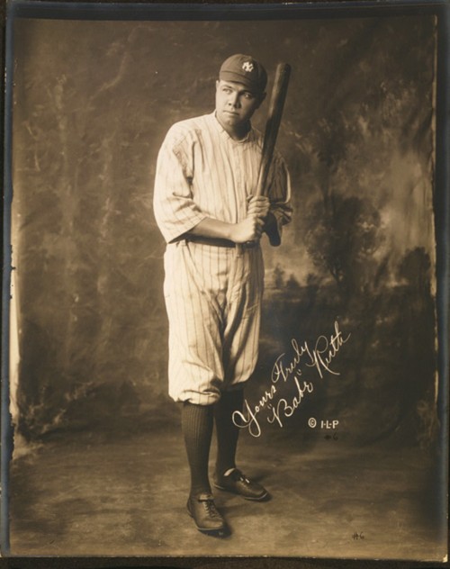 Photograph of Babe Ruth holding a baseball bat while wearing his New York Yankees uniform. 