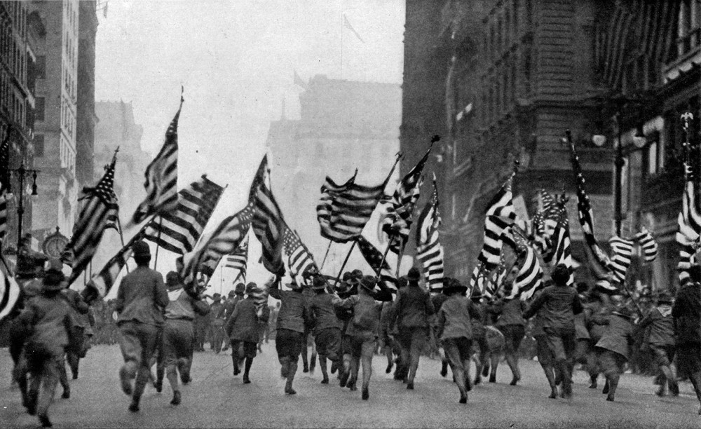 Dozens of Boy Scouts run up Fifth Avenue in New York City carrying large flags. 