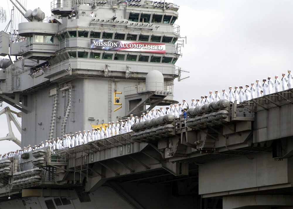 Photograph of a 2003 celebration aboard an aircraft carrier that featured a banner saying "MISSION ACCOMPLISHED"