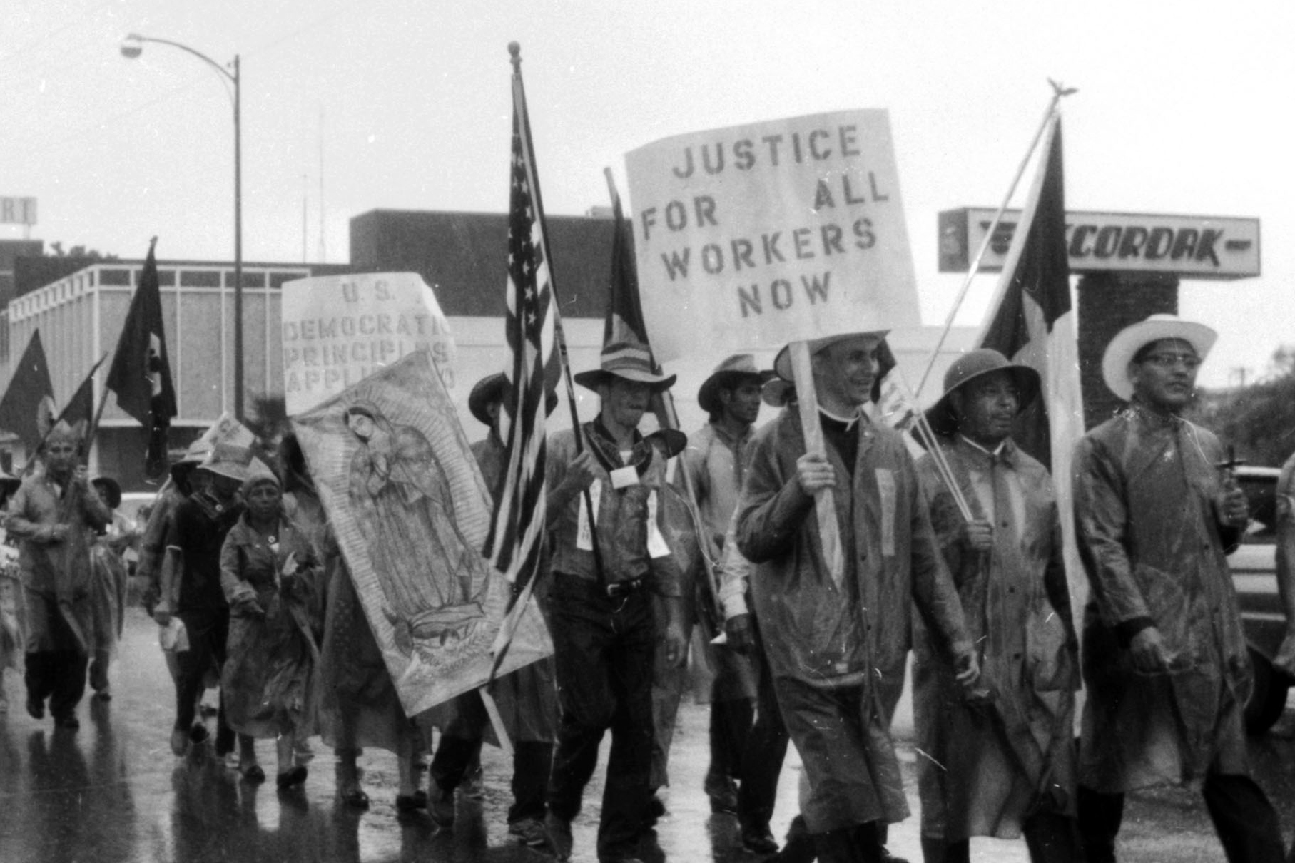 Photograph of the 1966 Rio Grande Valley Farm Workers March (“La Marcha”). Marchers hold the American flag, Texas flag, an image of the Virgin Mary, and signs that say "U.S. Democratic Principles Apply [unclear]," and "Justice for All Workers Now"