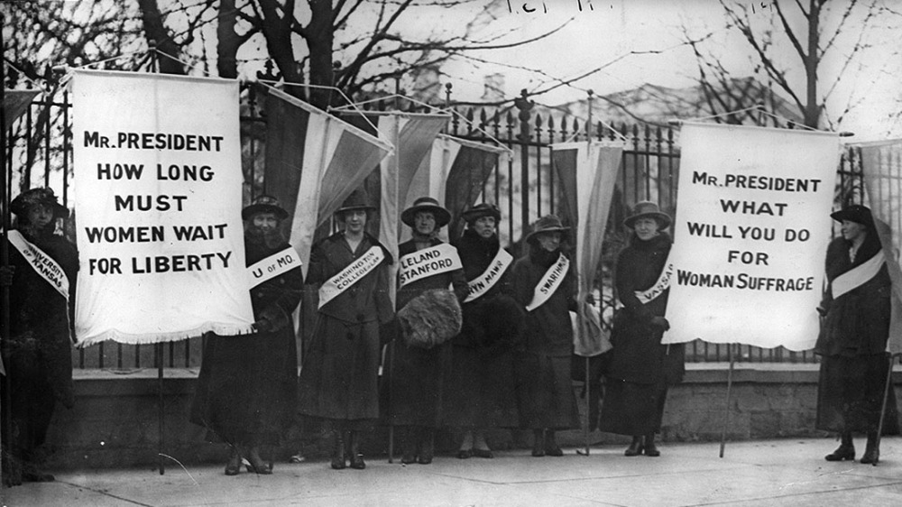 This photograph of suffragists shows women holding signs that say "Mr. President how long must women wait for liberty?" and "Mr. President what will you do for woman suffrage?"