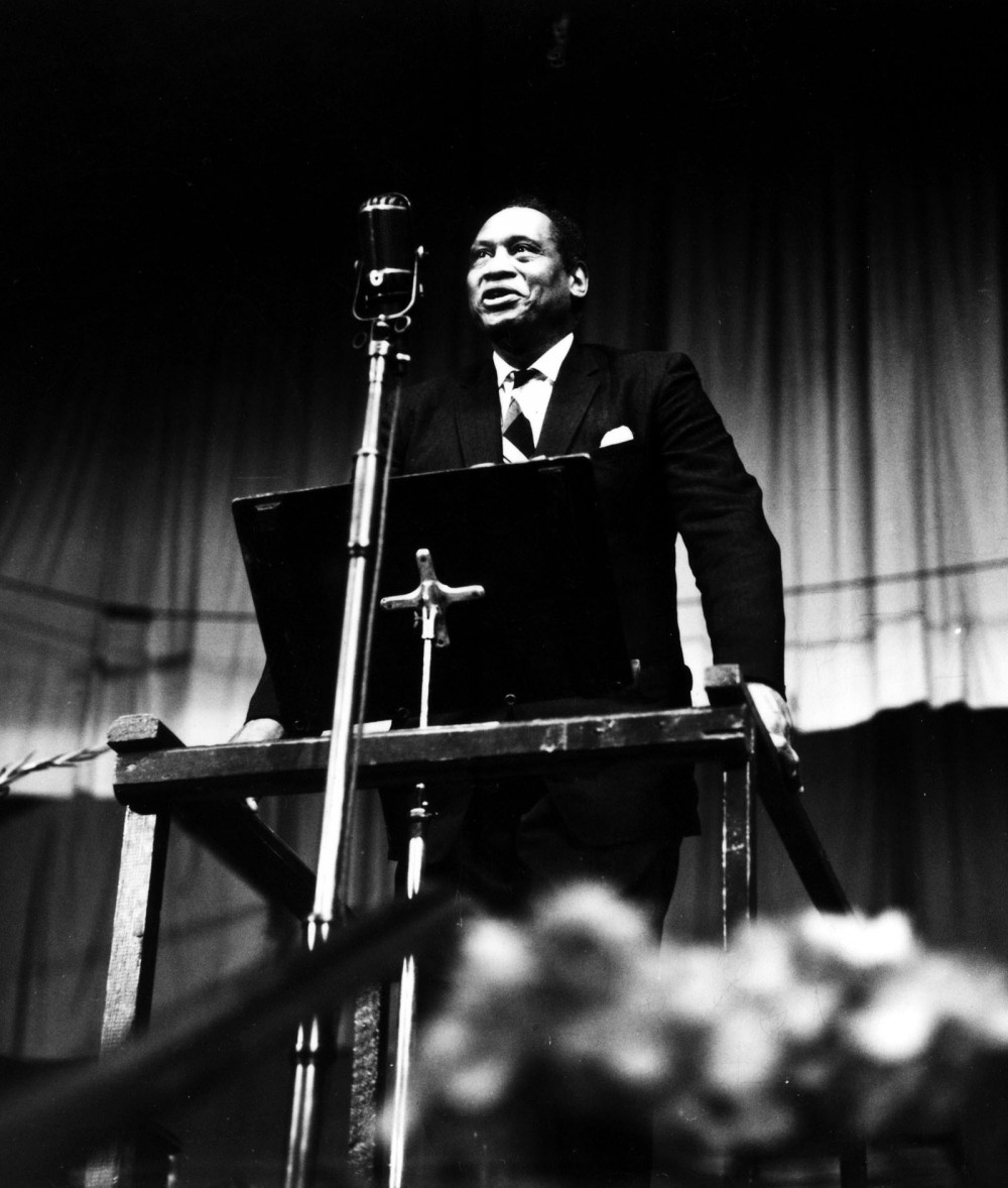 Photograph of Paul Robeson standing behind a lectern. 