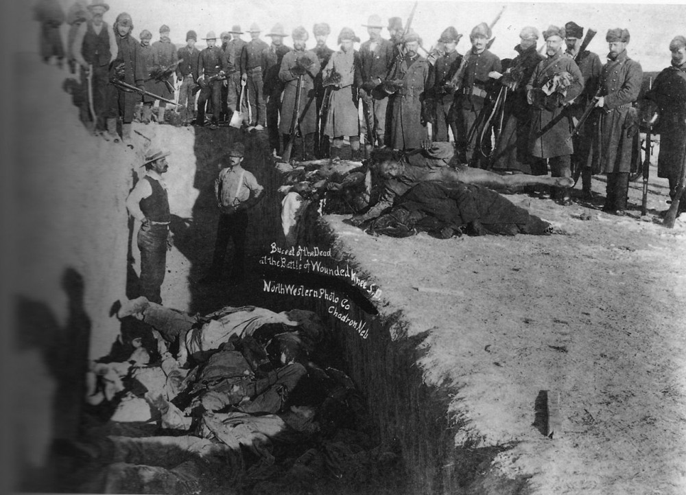 Burial of the dead after the massacre of Wounded Knee. U.S. Soldiers putting Indians in common grave; some corpses are frozen in different positions. South Dakota. 1891. Library of Congress.