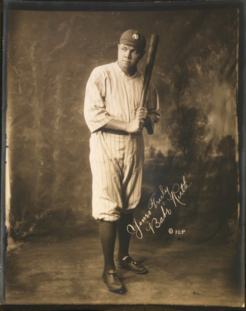 Photograph of Babe Ruth holding a baseball bat while wearing his New York Yankees uniform.