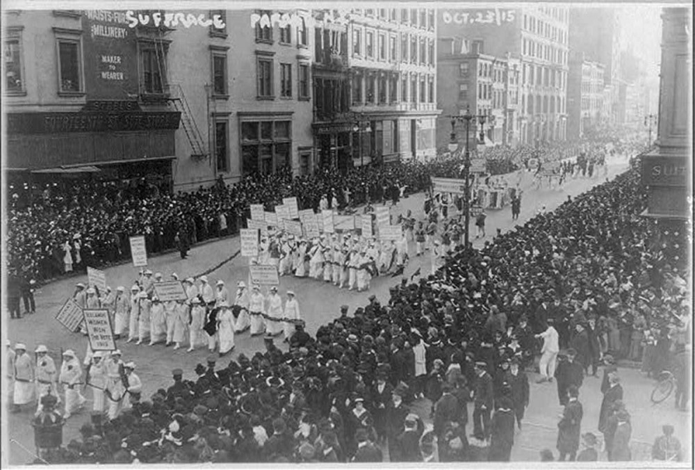 Photograph of suffragists marching in New York City in front of a sizable crowd. 
