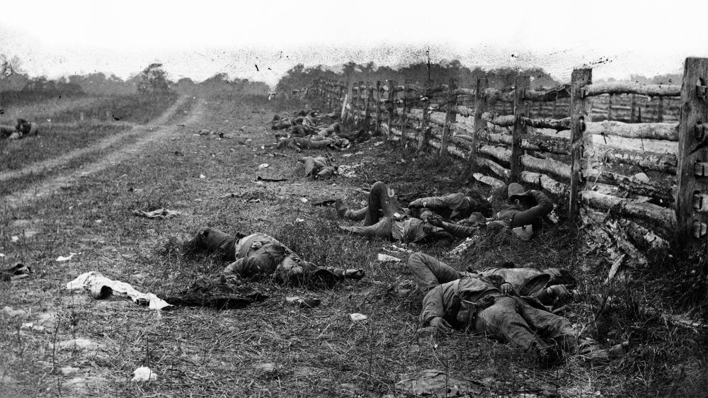 This photograph shows bodies strewn about near a fence. 