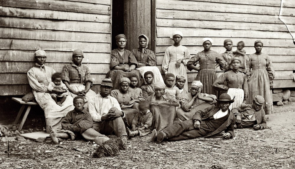 This photograph shows twenty three men, women, and children sitting together in a contraband camp.