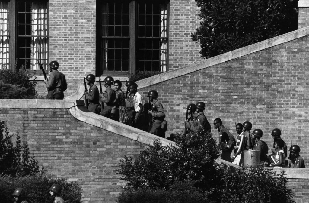 Soldiers escort students up the stairs of a high school.