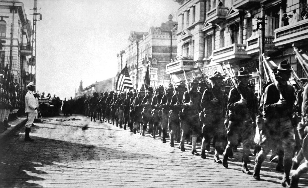 A column of soldiers marches through a city street.