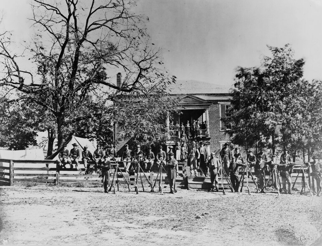 Union soldiers pose in front of the Appomattox Court House after Lee’s surrender in April 1865. The men stand in front of their weapons which are displayed together. The courthouse looms in the background. Wikimedia.
