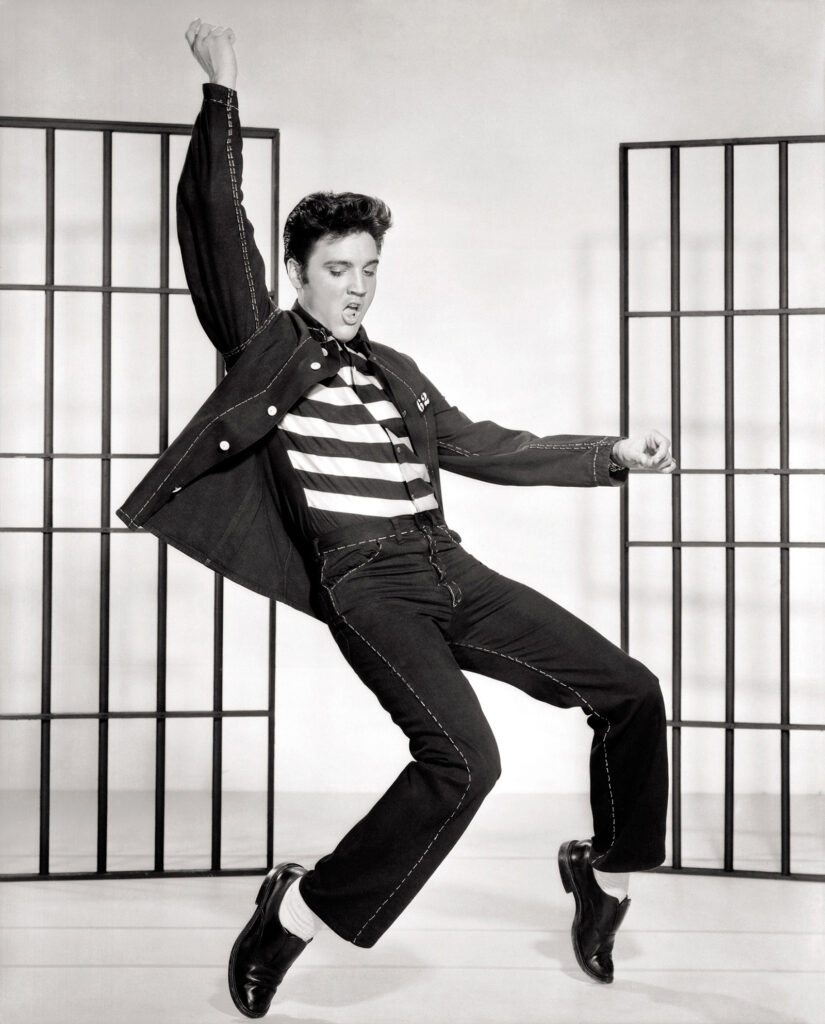 A man in a prison outfit dancing in front of iron jail doors.