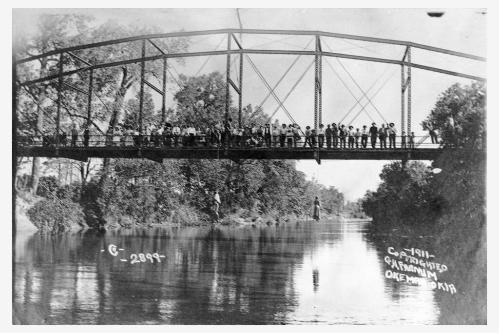 A crowd poses on an iron bridge with two bodies hanging below.