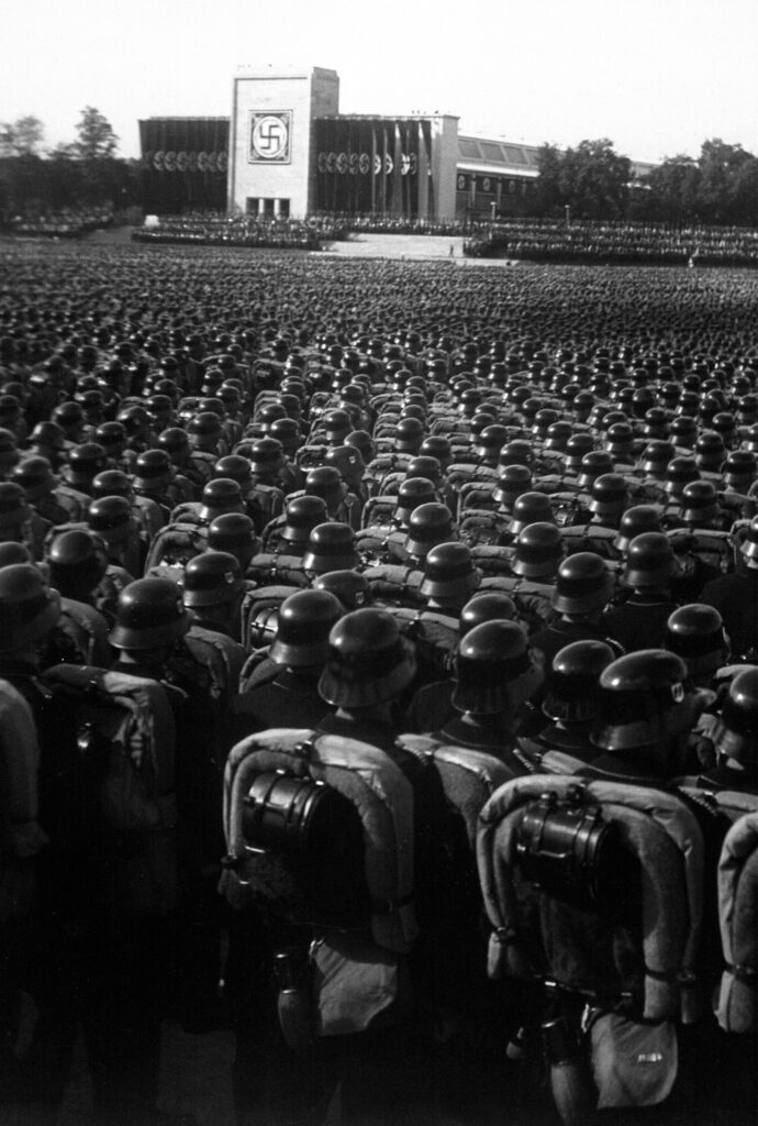 Legions of soldiers stand before a Nazi building. 