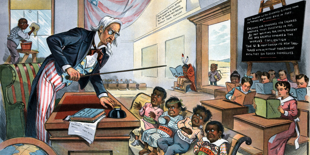 A political cartoon depicts Uncle Sam as a schoolmaster reprimanding dark-skinned children, representing the United States’s newly acquired territories, as well-behaved light skin children, representing U.S. states, read quietly behind them.