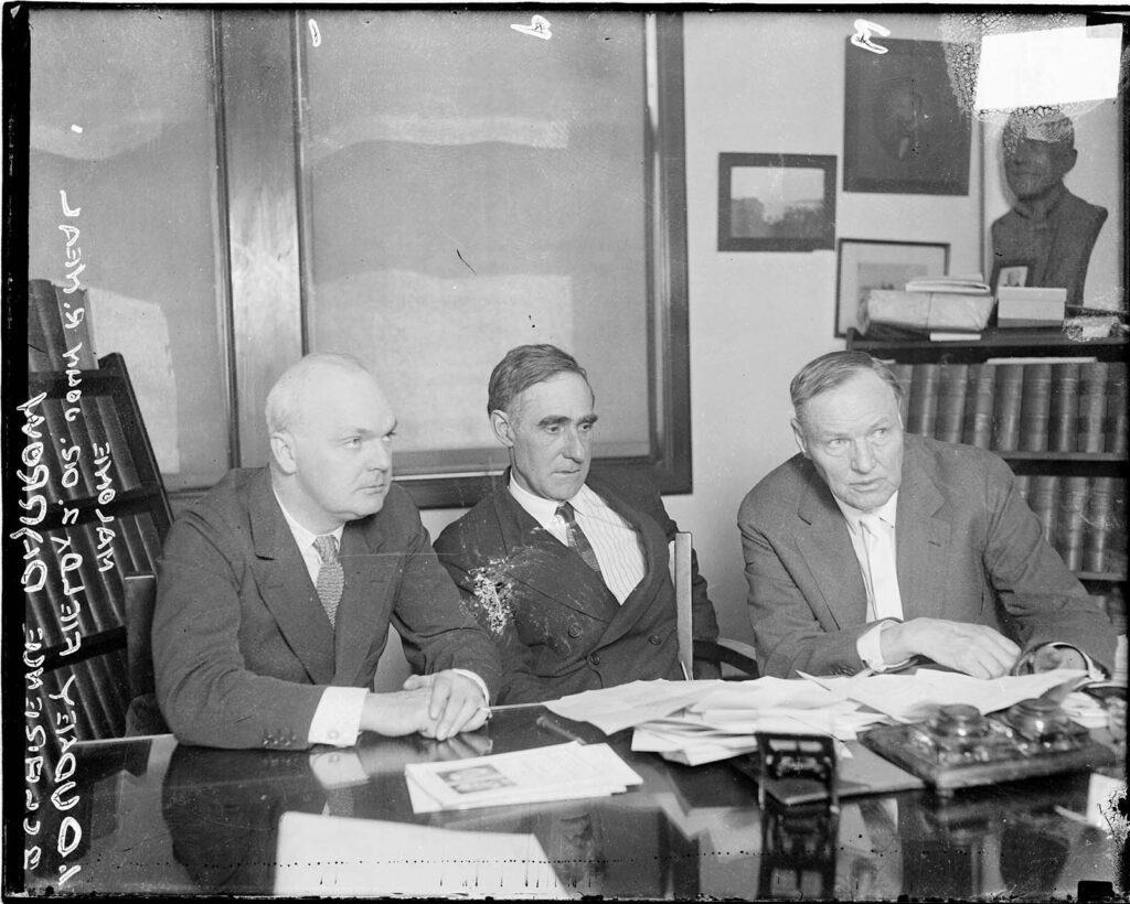 Three men sit at a desk.