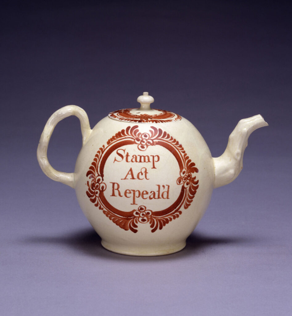 An eighteenth-century British colonial teapot. The teapot is white with a red pattern and red lettering that reads, “Stamp Act Repeal’d.”