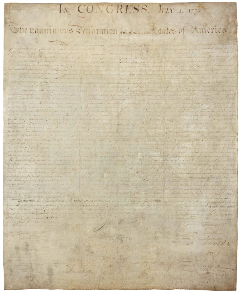 A faded image of the declaration of independence. The writing is indecipherable outside of the top two lines that read, “In Congress, July 4, 1776. The unanimous Declaration of the thirteen unified States of America.”