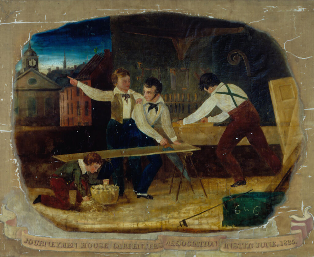 A Carpenter points to a clock tower informing his colleagues that it is time for them to quit work for the day. He has his hand on another carpenter’s shoulder, who is sawing through a plank of wood, in the center of the artwork. In the foreground another carpenter picks up wood shavings off the ground, placing them in a basket. In the background, another carpenter continues to work on a piece of wood, facing away from his fellow carpenters in the center of the scene. Several carpentry tools hang on the wall in the background of the scene.